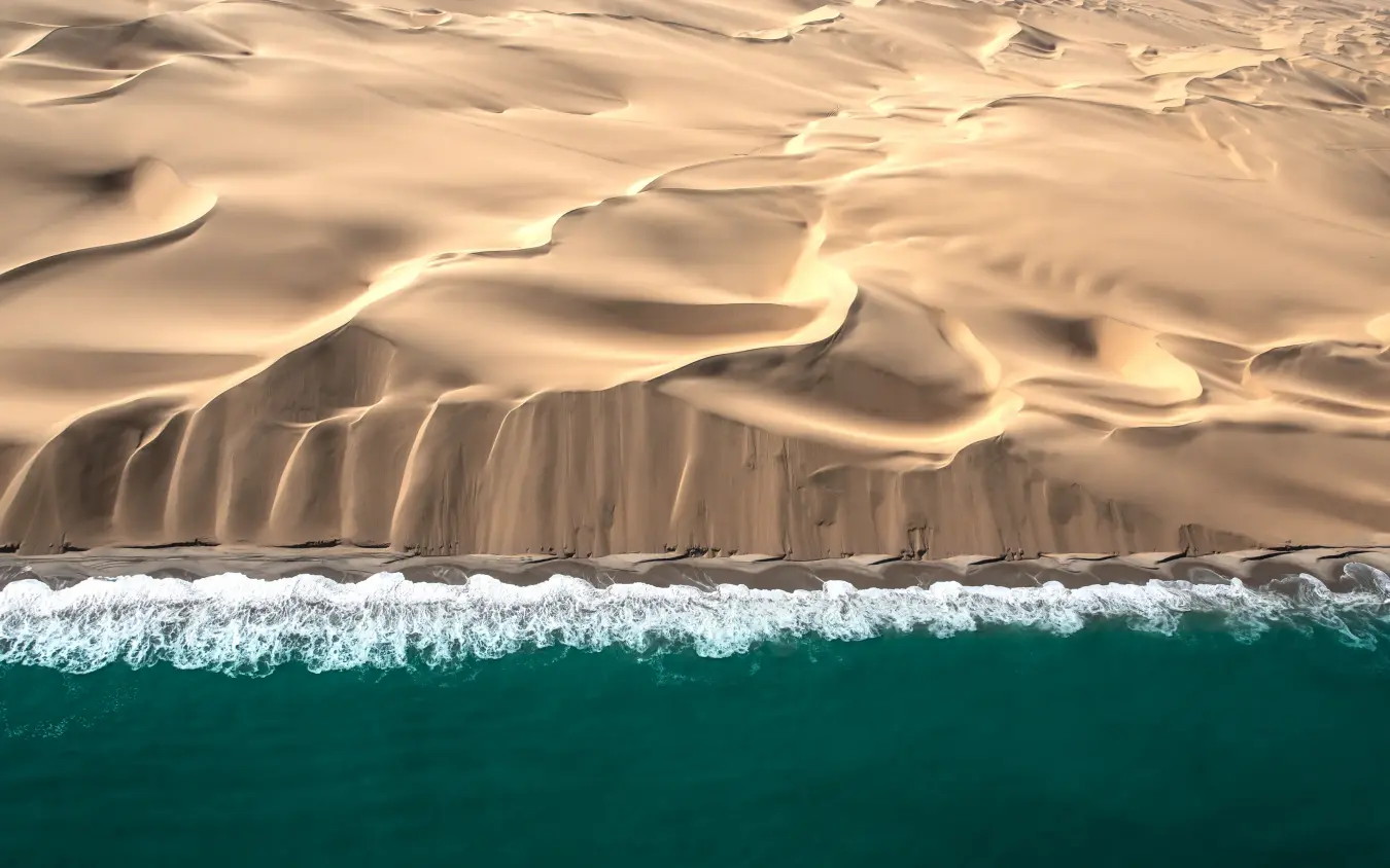 Aerial view of desert meeting ocean with white waves