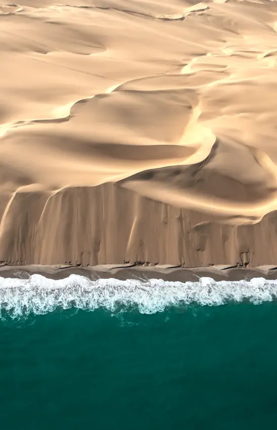 Aerial view of desert meeting ocean with white waves