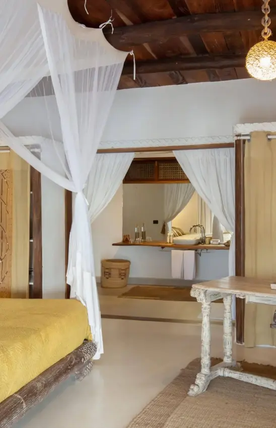 Luxurious bedroom suite with canopy bed and en-suite bathroom visible through sheer curtains, Alfajiri Beach Villa, Diani Beach, Kenya