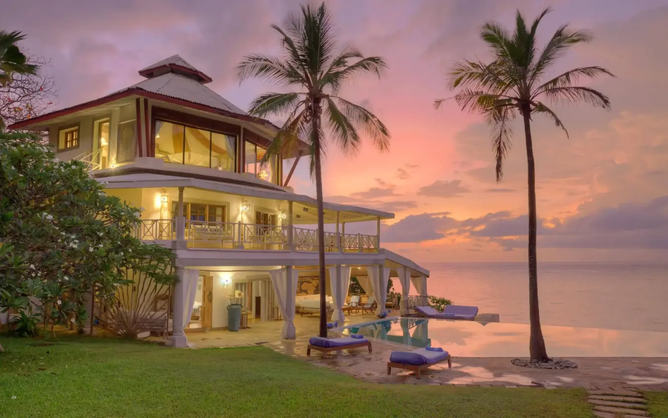 Beachfront villa with illuminated interiors at sunset with palm trees, Alfajiri Cliff Villa, Diani Beach, Kenya
