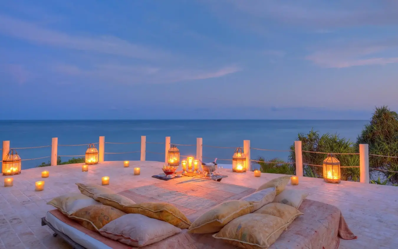 Beachfront terrace with floor cushions and lanterns at dusk overlooking ocean, Alfajiri Garden Villa, Diani Beach, Kenya