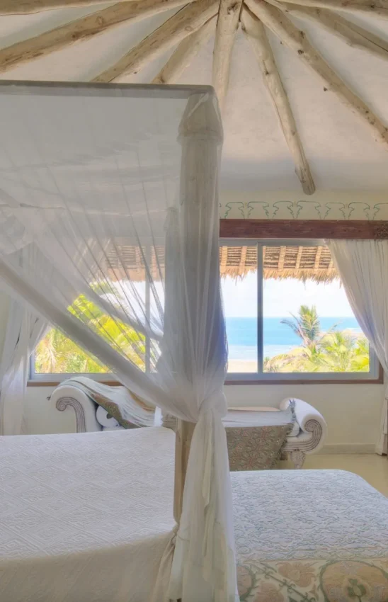 Beachfront bedroom with four-poster bed and ocean view through windows, Alfajiri Garden Villa, Diani Beach, Kenya