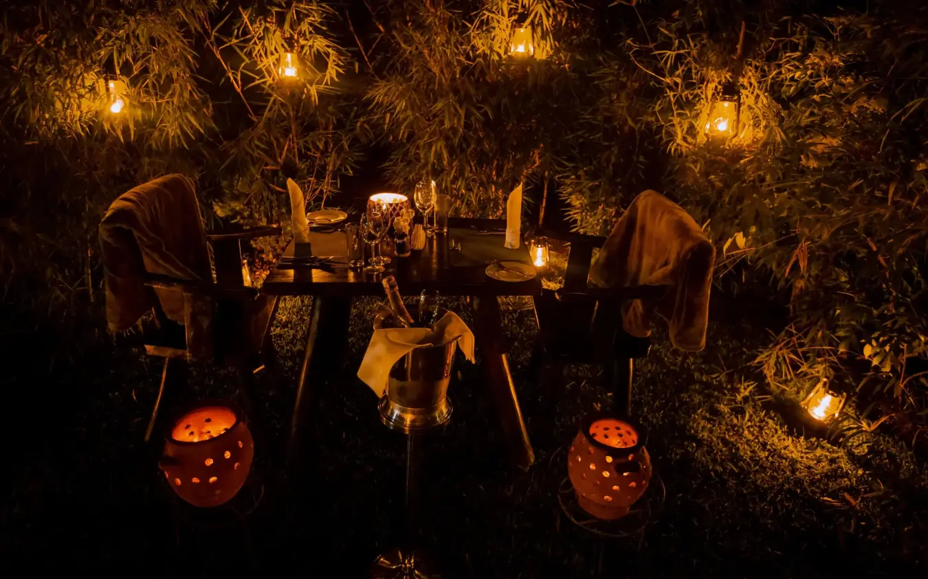 Outdoor dining table set under hanging lanterns at night, Amakoro Songa Lodge, Volcanoes National Park, Rwanda