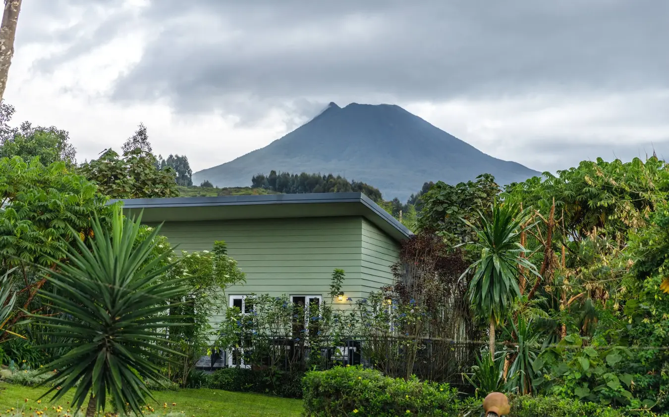 Green lodge building with mountain backdrop and tropical gardens, Amakoro Songa Lodge, Volcanoes National Park, Rwanda