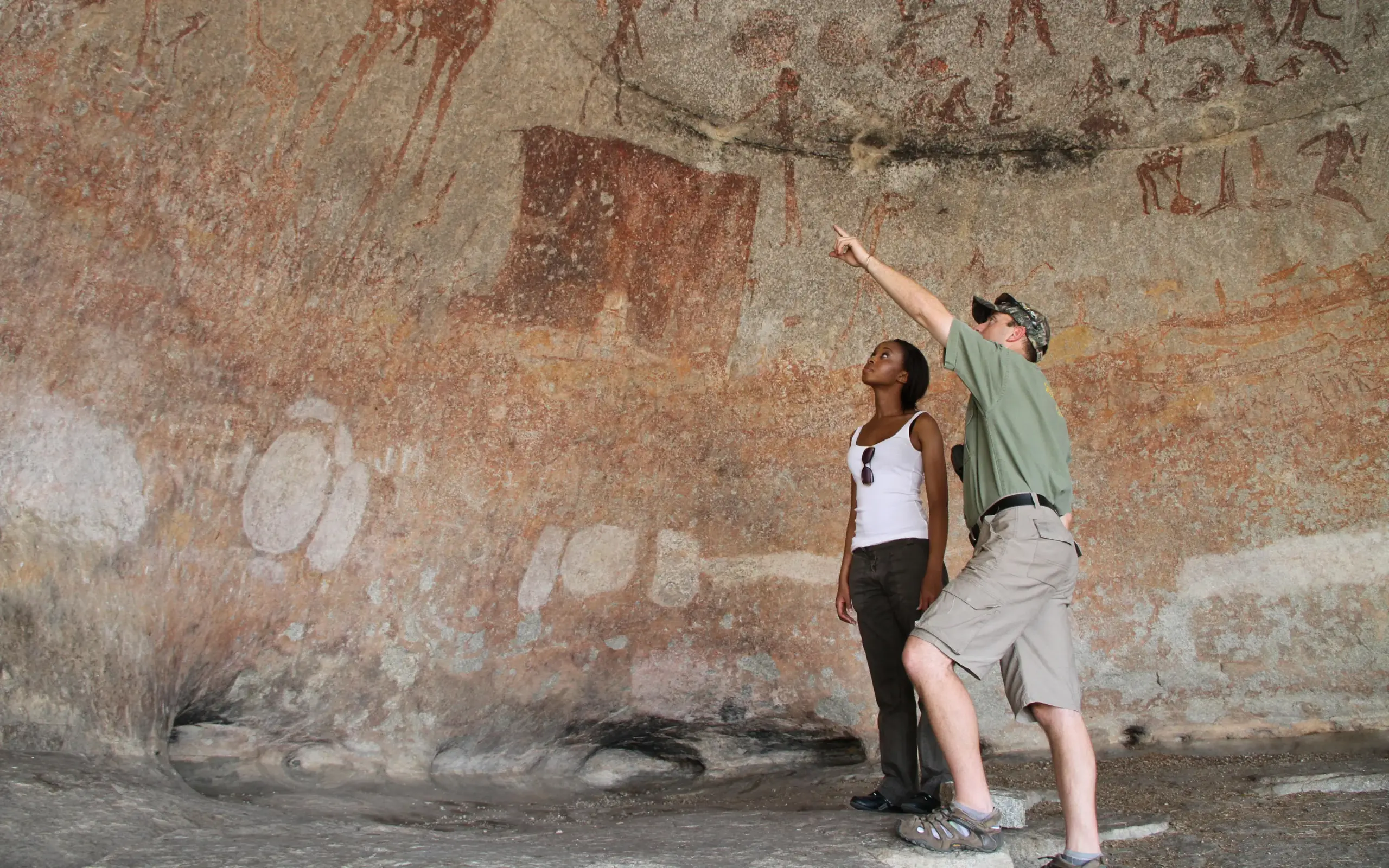 Guests examining ancient rock art on stone wall, Matobo, Zimbabwe
