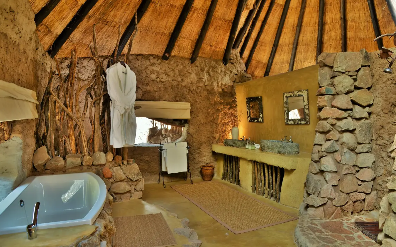Rustic stone bathroom with thatched roof and soaking tub, Amalinda Lodge, Matobo, Zimbabwe