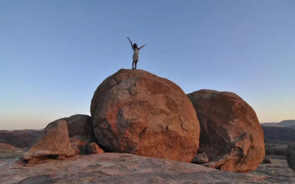 Person standing on large balanced rock formations at sunset, Amalinda Lodge, Matobo, Zimbabwe