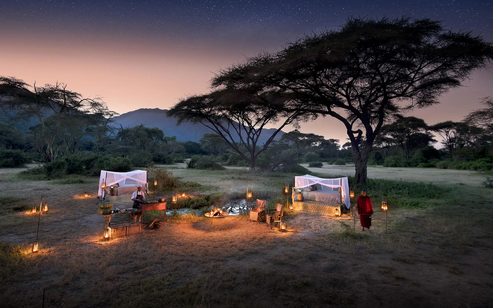 Candlelit outdoor dining setup under acacia trees at dusk, Lake Manyara Tree Lodge, Lake Manyara, Tanzania