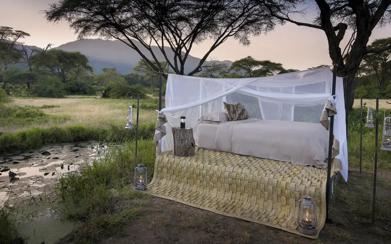 Bed with mosquito netting overlooking stream and acacia trees, Lake Manyara Tree Lodge, Lake Manyara, Tanzania