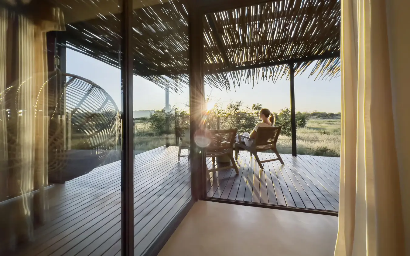 Guest relaxing on wooden deck at sunset overlooking savanna, Anderssons at Ongava, Etosha National Park, Namibia