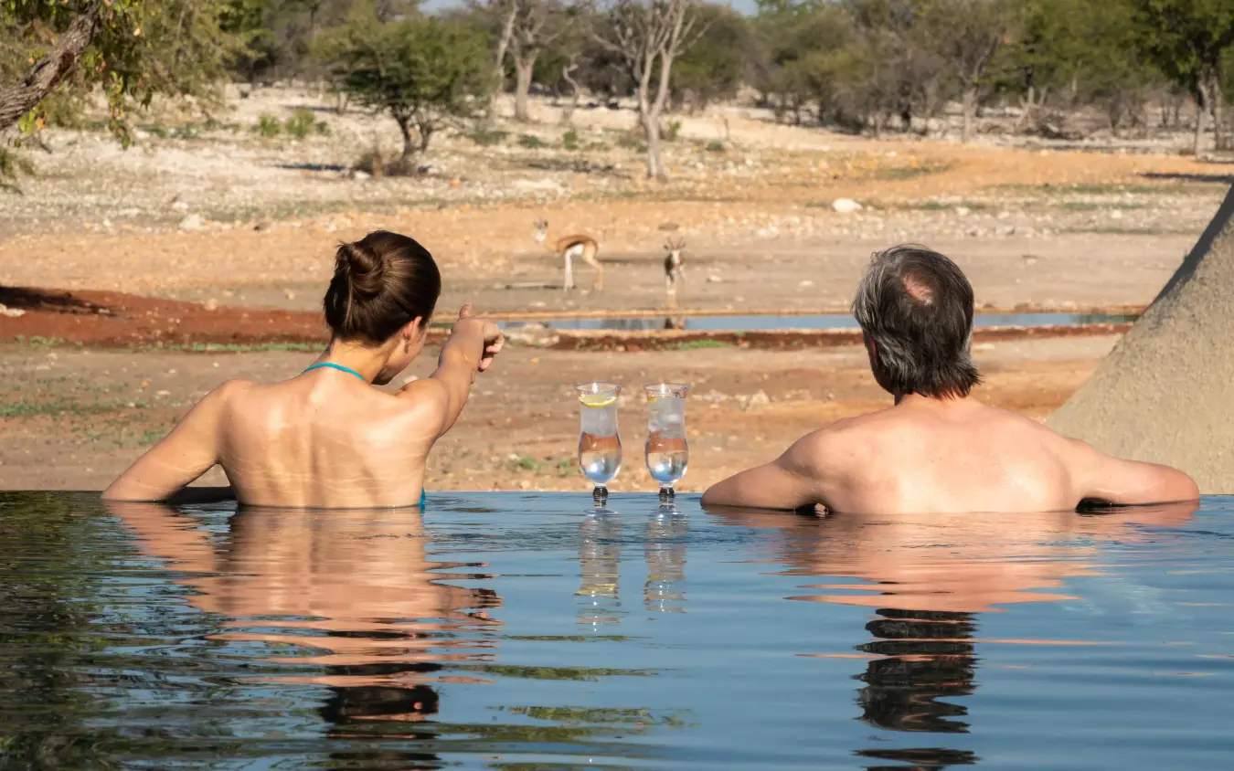 Guests relaxing in waterhole pool overlooking wildlife area, Anderssons at Ongava, Etosha National Park, Namibia