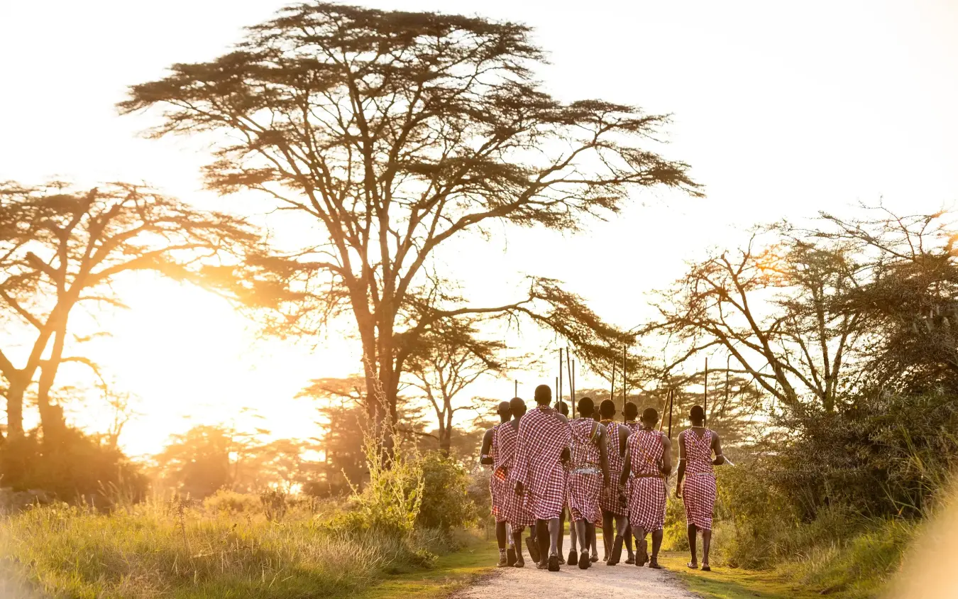 Group of people in traditional dress walking on dirt road at sunset, Angama Amboseli, Amboseli and Chyulu Hills, Kenya