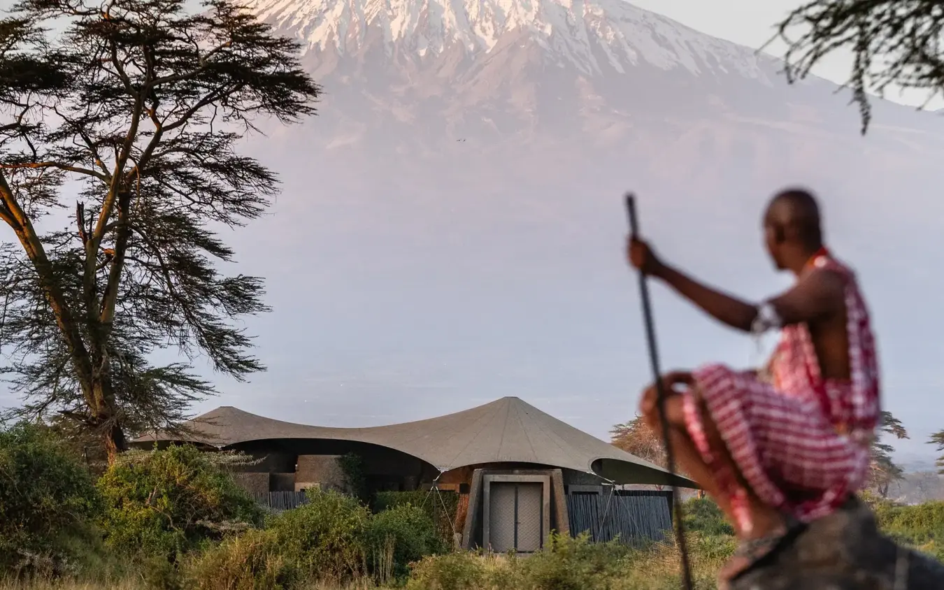 Maasai warrior with spear beside luxury safari lodge and snow-capped mountain, Angama Amboseli, Amboseli and Chyulu Hills, Kenya