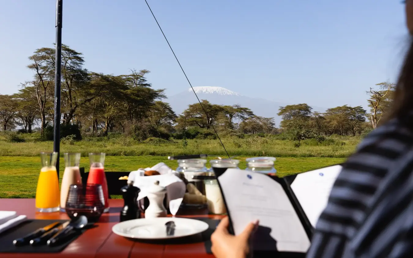 Outdoor dining table with snow-capped mountain view across savanna grassland, Angama Amboseli, Amboseli and Chyulu Hills, Kenya