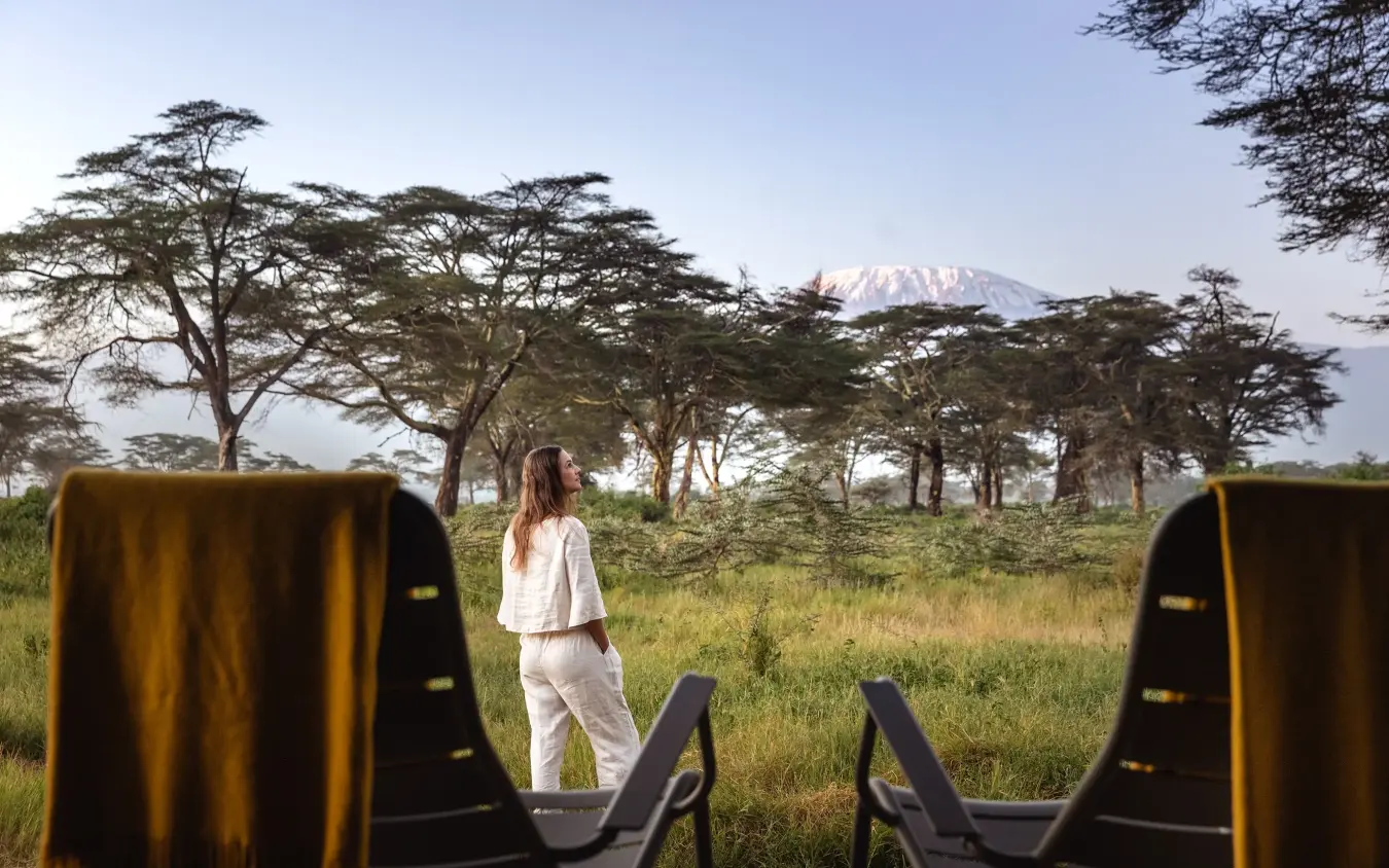 Woman in white standing in grassland with acacia trees and snow-capped mountain, Angama Amboseli, Amboseli and Chyulu Hills, Kenya