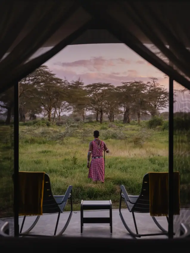 Woman in traditional dress standing in grassland viewed from safari lodge, Angama Amboseli, Amboseli and Chyulu Hills, Kenya