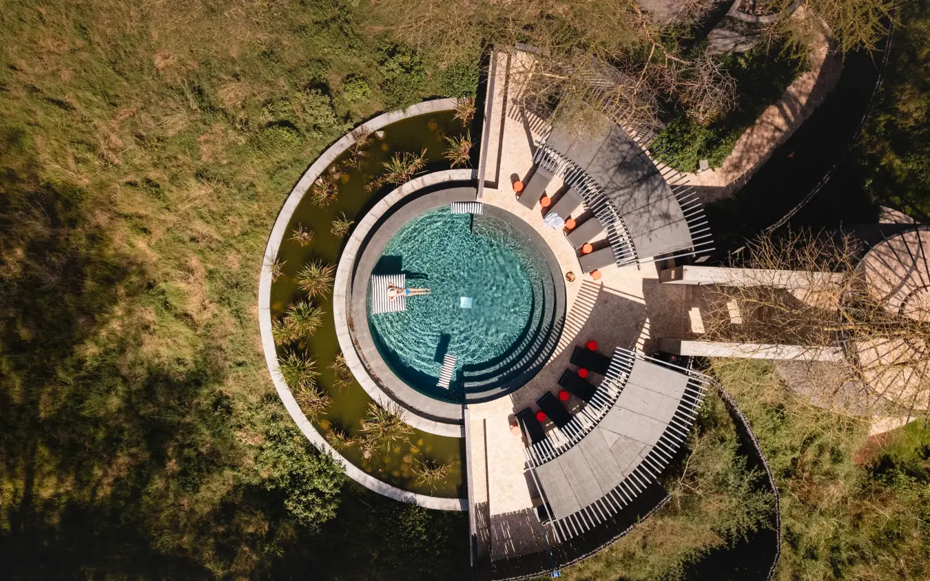 Circular modern pool with loungers surrounded by woodland forest from above, Angama Amboseli, Amboseli and Chyulu Hills, Kenya