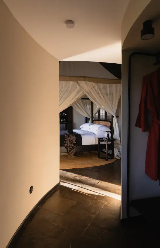 Luxury bedroom suite with cream draped four-poster bed viewed through curved archway, Angama Amboseli, Amboseli and Chyulu Hills, Kenya