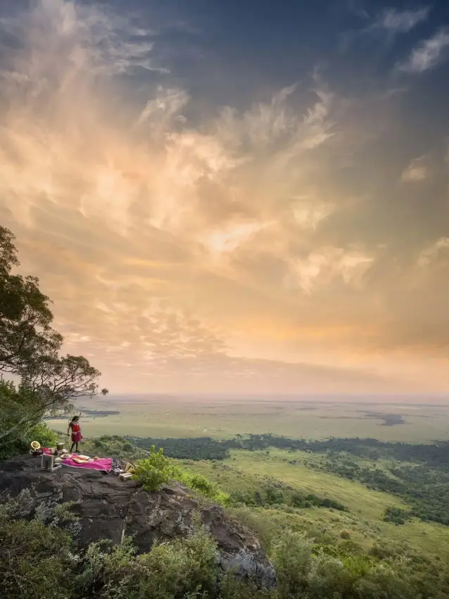 Guest on rocky outcrop overlooking expansive savanna valley, Angama Mara, Maasai Mara, Kenya