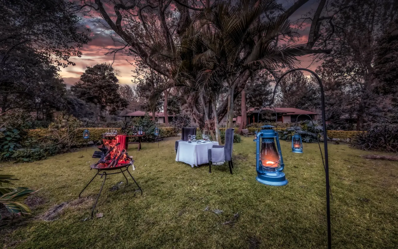 Outdoor evening gathering with fire pit and lanterns in garden setting, Arusha Coffee Lodge, Arusha, Tanzania