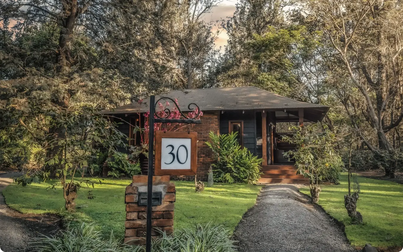 Brick lodge entrance with number 30 sign among tall trees and manicured gardens, Arusha Coffee Lodge, Arusha, Tanzania