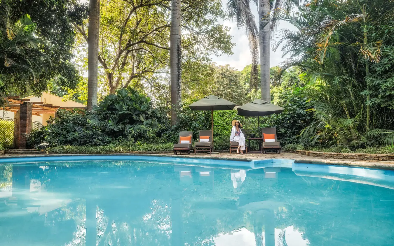 Woman relaxing by turquoise swimming pool surrounded by tropical gardens and palm trees, Arusha Coffee Lodge, Arusha, Tanzania