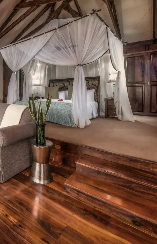 Luxury canopy bed with sheer curtains in rustic timber bedroom interior, Arusha Coffee Lodge, Arusha, Tanzania
