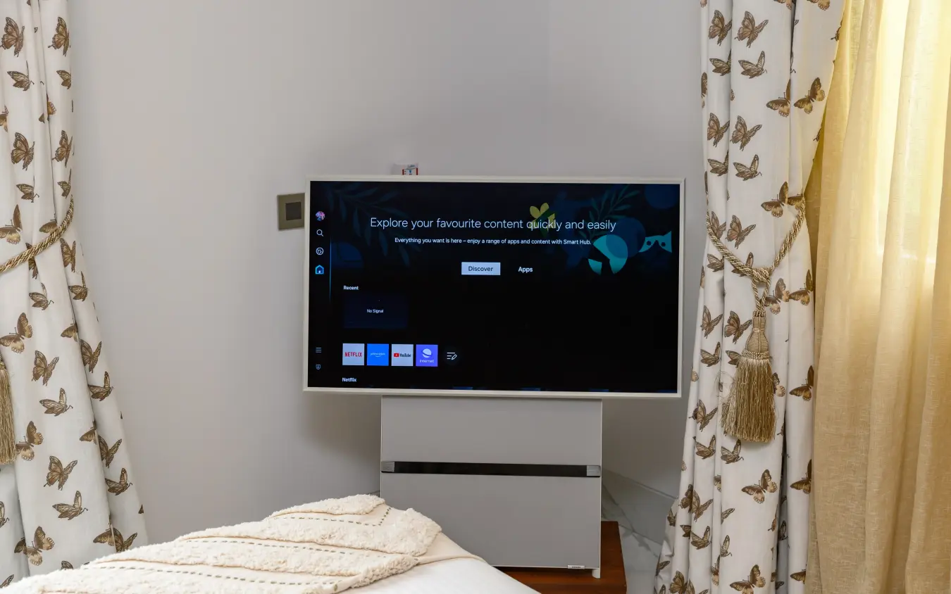 Flat-screen television mounted above bed in guest bedroom with patterned curtains, Bahari Bliss, Kilifi, Kenya
