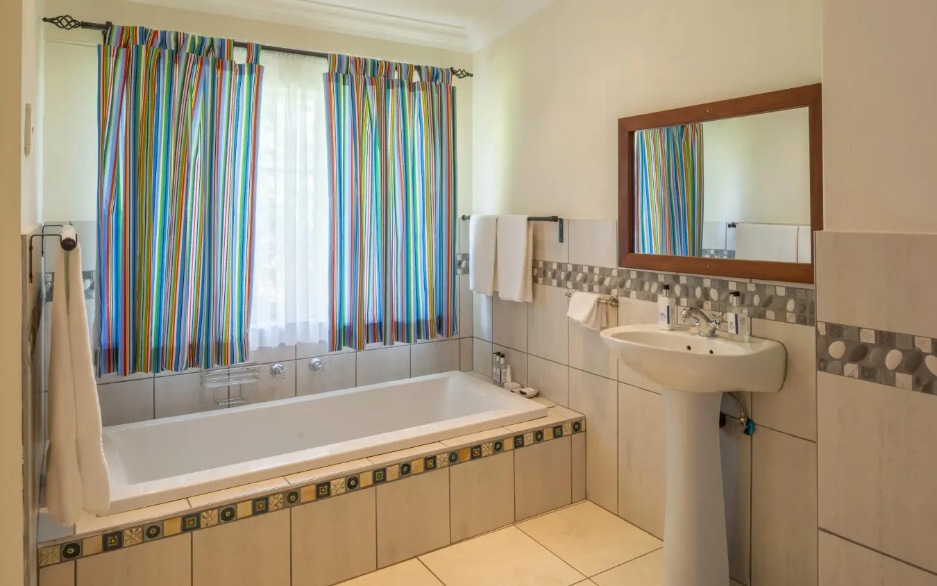 Modern bathroom with bathtub, sink, and colorful striped curtains, Batonka Guest Lodge, Victoria Falls, Zimbabwe