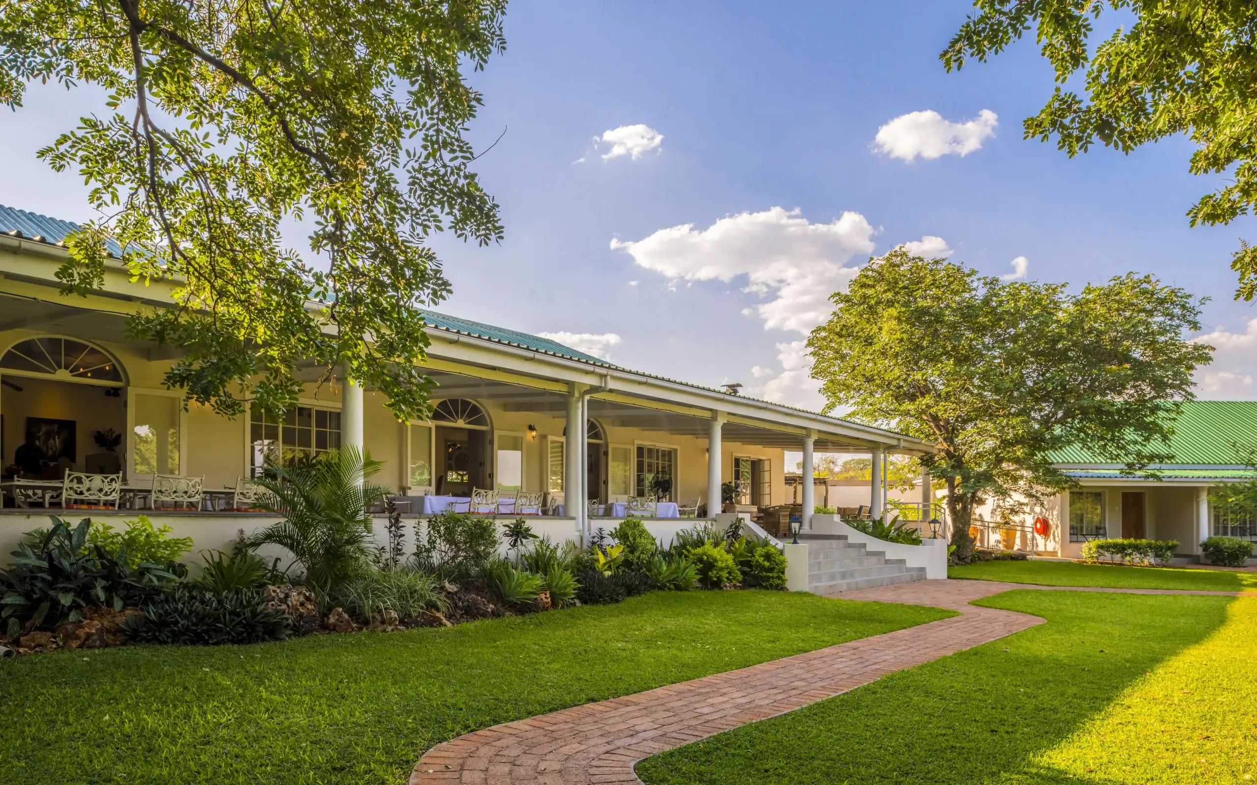 Yellow colonial-style building with manicured lawn and trees, Batonka Guest Lodge, Victoria Falls, Zimbabwe