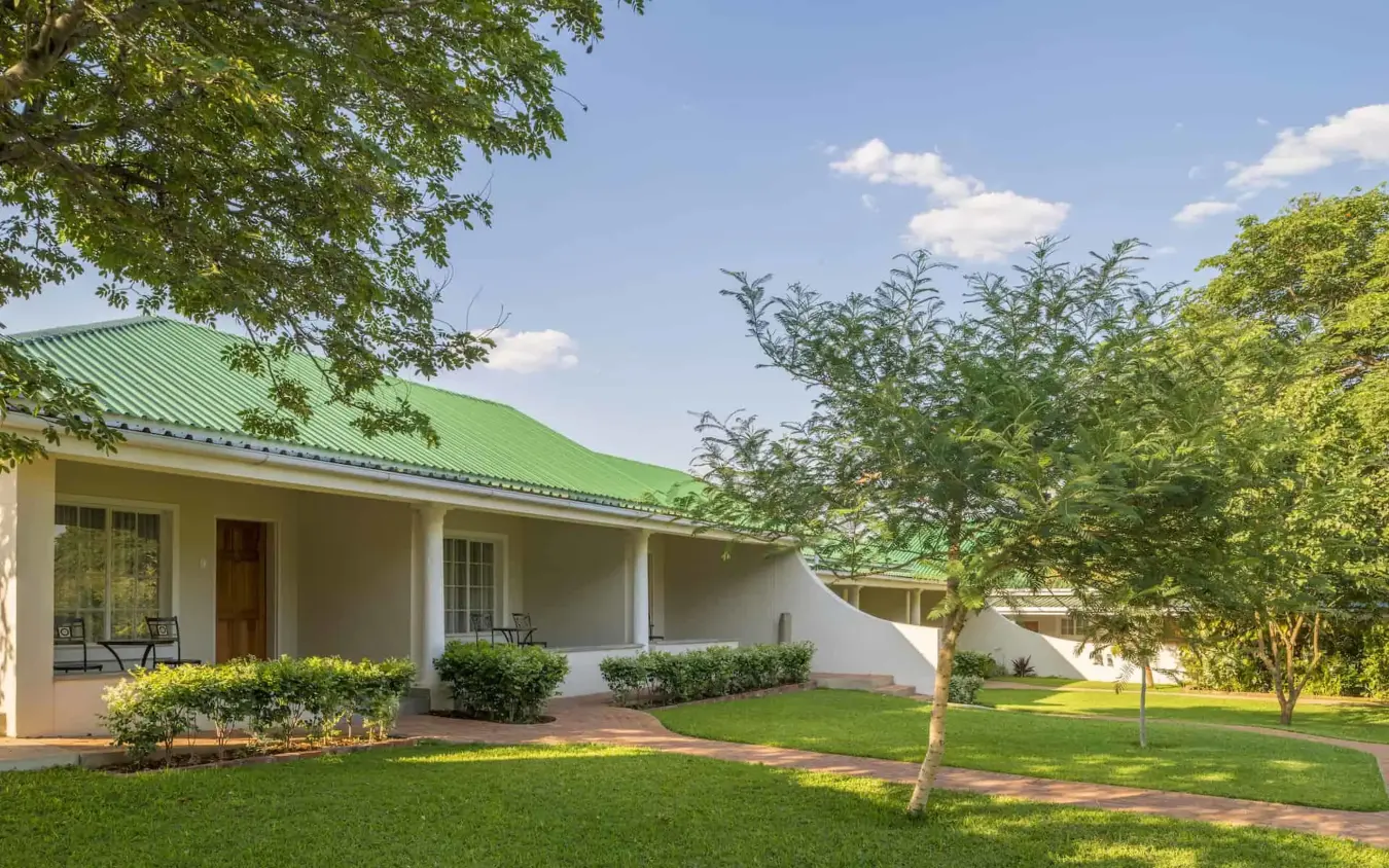 White farmhouse with green metal roof and manicured grounds, Batonka Guest Lodge, Victoria Falls, Zimbabwe