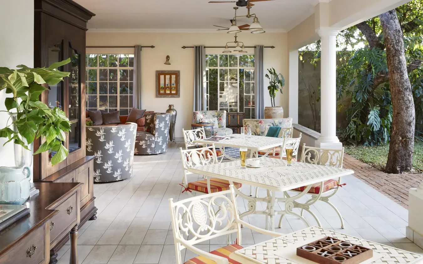 Covered porch with seating areas and large windows overlooking garden, Batonka Guest Lodge, Victoria Falls, Zimbabwe