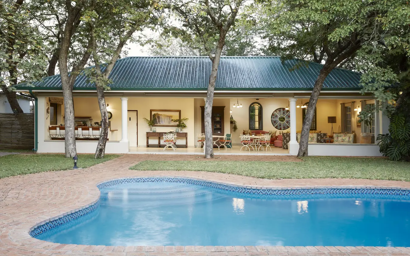 Swimming pool with lodge building and mature trees behind, Batonka Guest Lodge, Victoria Falls, Zimbabwe