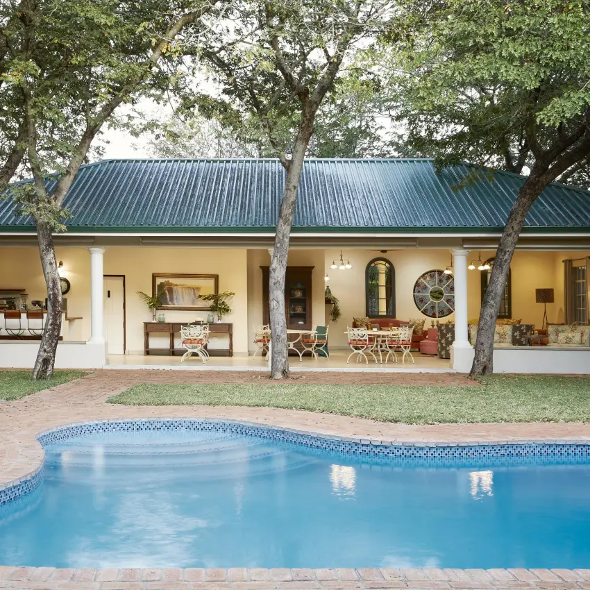 Swimming pool with lodge building and mature trees behind, Batonka Guest Lodge, Victoria Falls, Zimbabwe