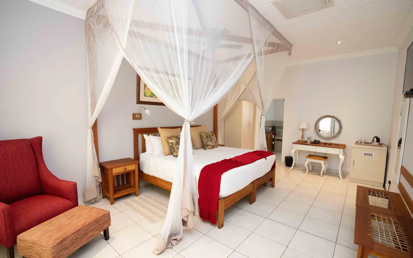Spacious bedroom with four-poster canopy bed and seating area, Batonka Guest Lodge, Victoria Falls, Zimbabwe