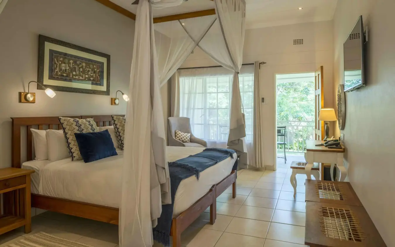 Spacious bedroom with four-poster bed and seating area, Batonka Guest Lodge, Victoria Falls, Zimbabwe
