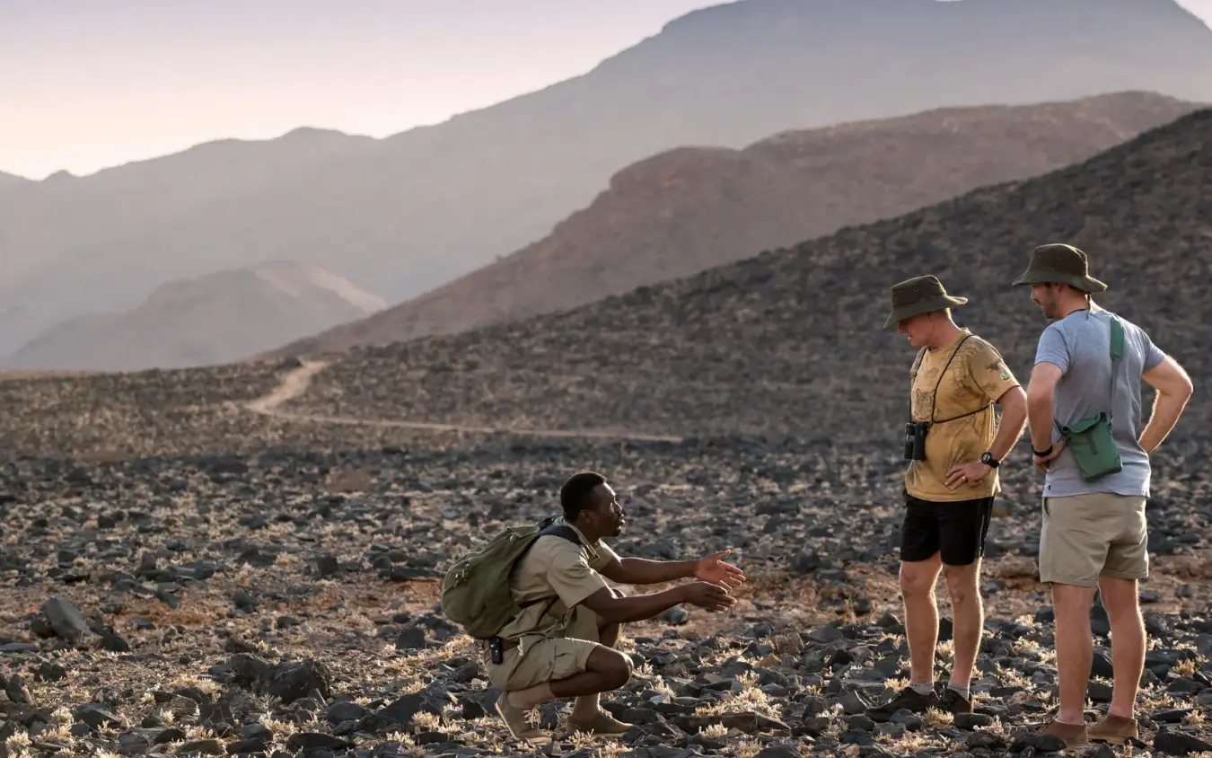 Guide explaining desert geology to two guests during walking tour, Sossusvlei Desert Lodge, NamibRand Private Reserve, Namibia