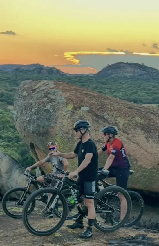 Mountain bikers with helmets posing at large rock formation at sunset, Big Cave Camp, Matobo, Zimbabwe