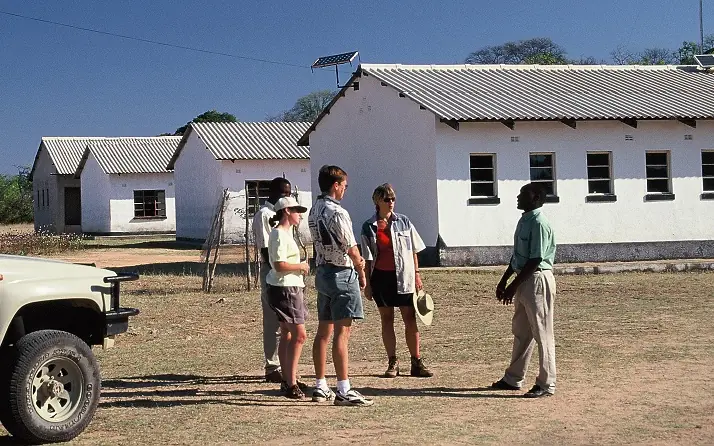 Guests standing beside safari vehicle at white lodge buildings, Big Cave Camp, Matobo, Zimbabwe