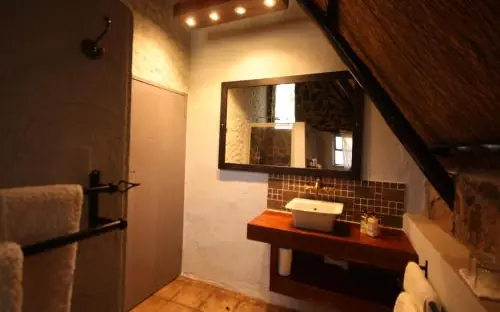 Luxury bathroom vanity with mirror and warm lighting in lodge suite, Big Cave Camp, Matobo, Zimbabwe