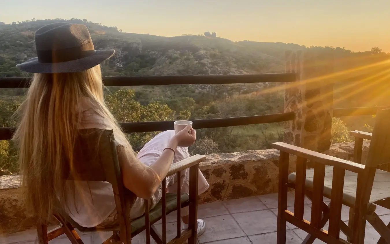 Woman with long blonde hair enjoying sunset view from wooden deck overlooking valley, Big Cave Camp, Matobo, Zimbabwe
