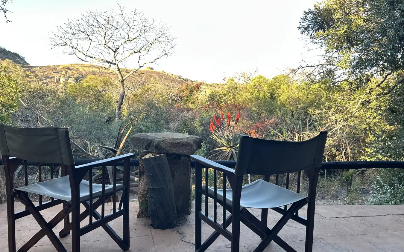 Two director chairs at wooden table overlooking bushveld landscape, Big Cave Camp, Matobo, Zimbabwe