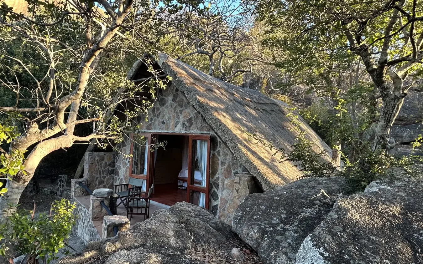 Stone cottage with thatched roof nestled among rocky outcrops and trees, Big Cave Camp, Matobo, Zimbabwe
