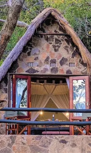 Stone lodge with thatched roof nestled among forest trees, Big Cave Camp, Matobo, Zimbabwe