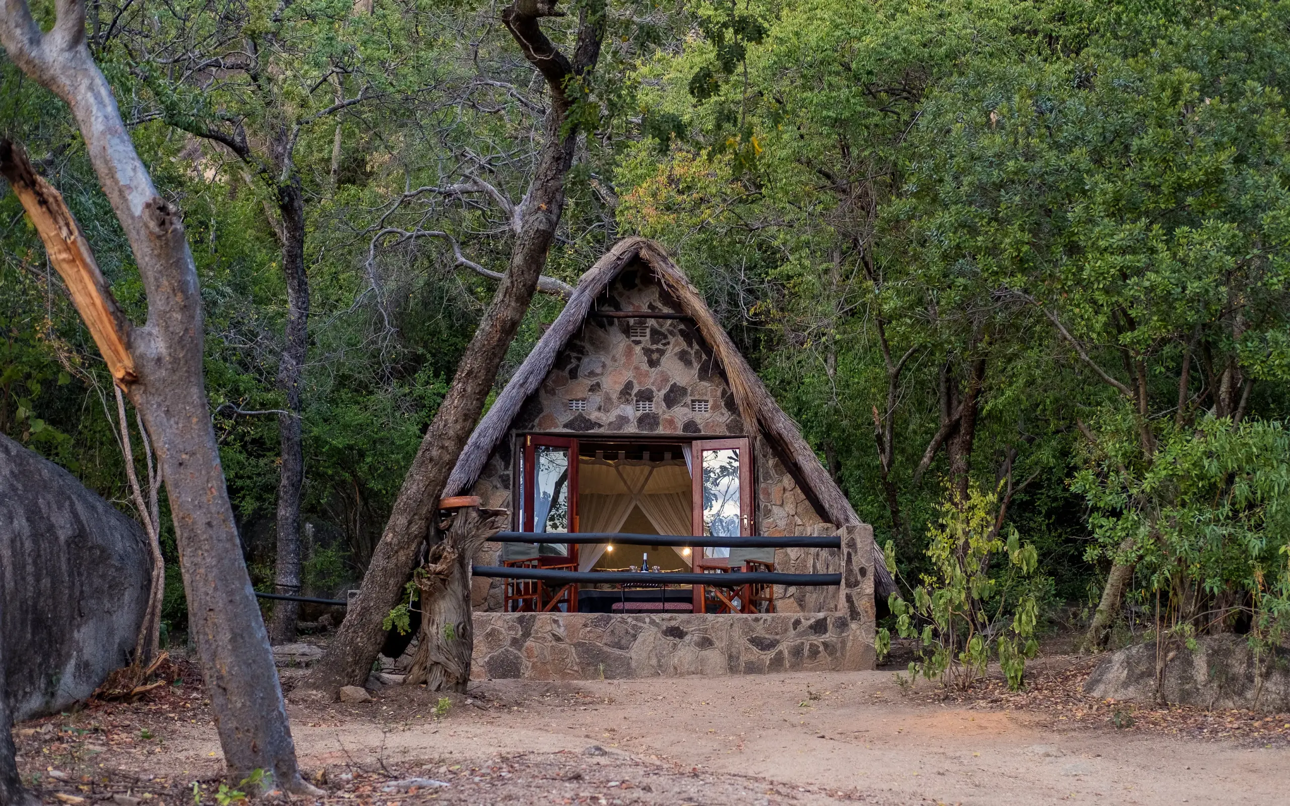 Stone bungalow with thatched roof nestled among forest trees, Big Cave Camp, Matobo, Zimbabwe