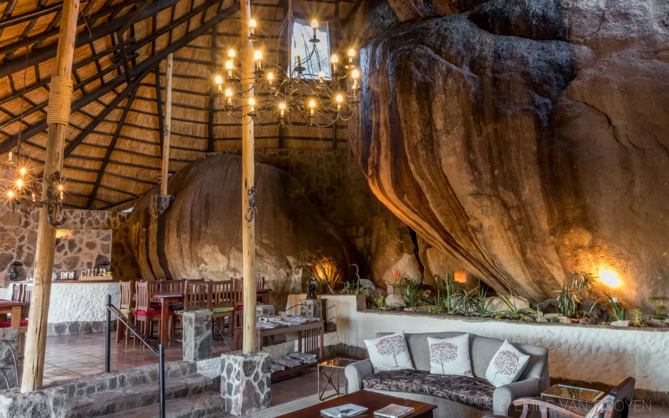 Luxury lounge carved beneath massive rock boulders with warm lighting, Big Cave Camp, Matobo, Zimbabwe