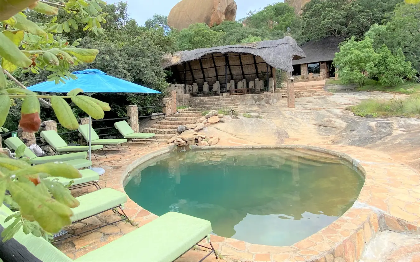 Natural stone pool with loungers and thatched structures in bush setting, Big Cave Camp, Matobo, Zimbabwe