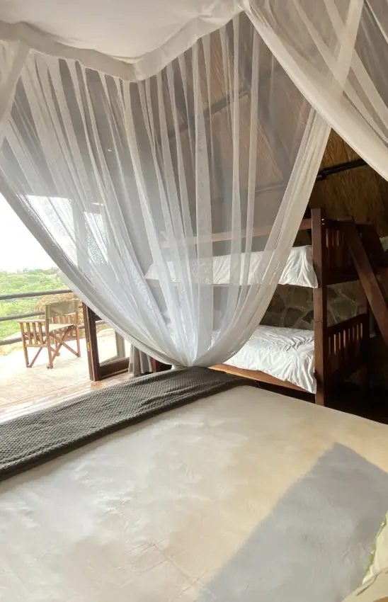 Canopied bed with sheer drapes overlooking savanna landscape from wooden deck, Big Cave Camp, Matobo, Zimbabwe