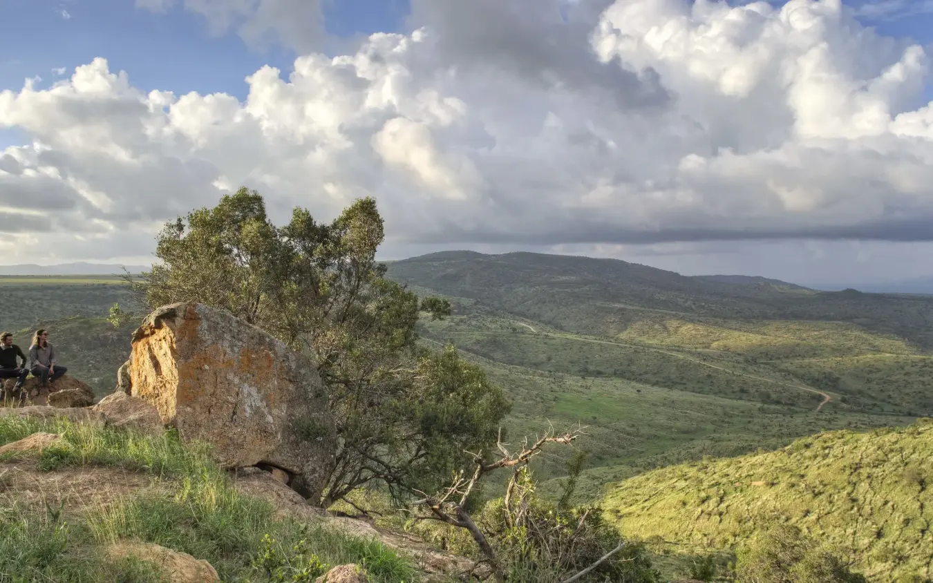 Guests hiking on hillside overlooking green valley landscape, Borana Lodge, Laikipia Highlands, Kenya