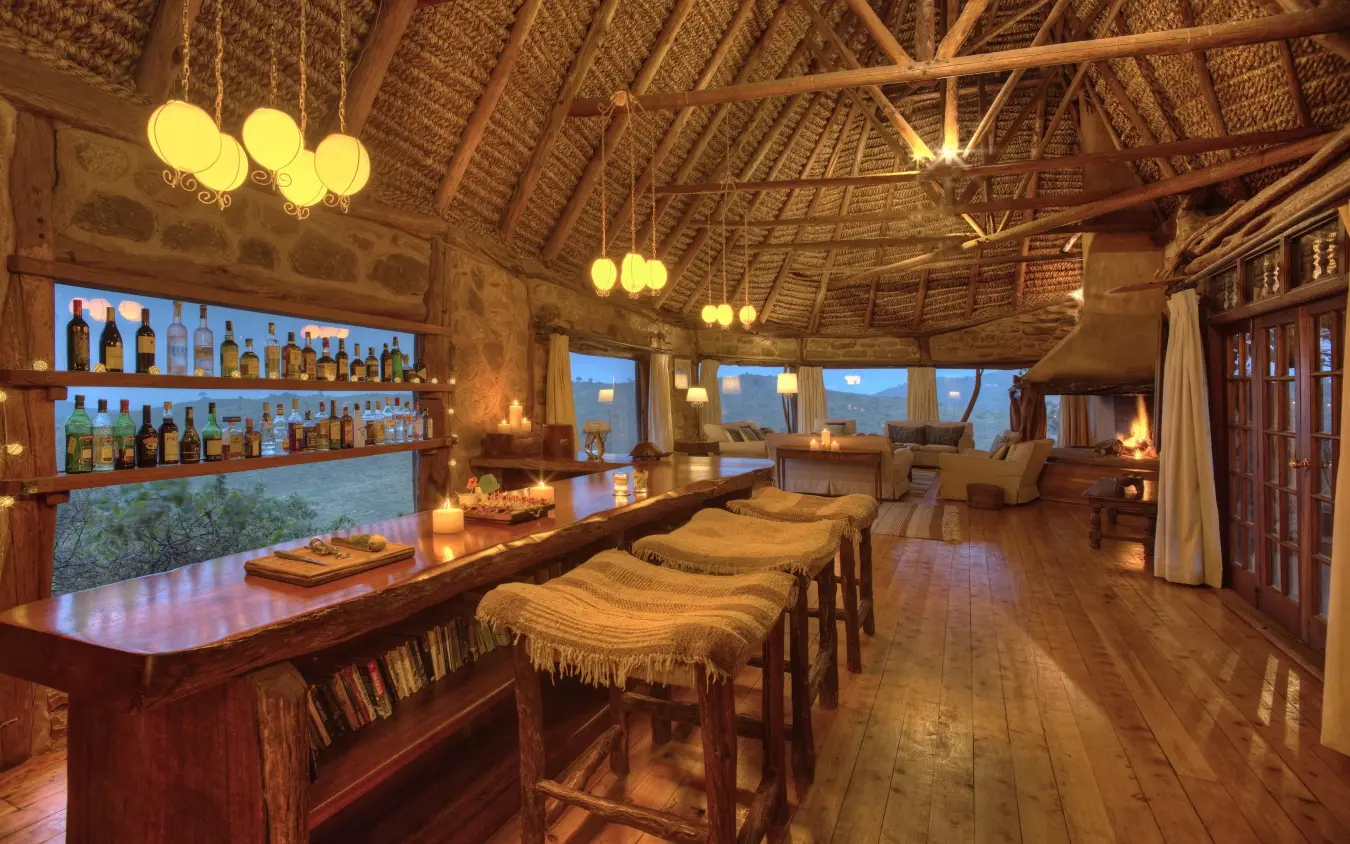 Thatched lounge with bar, seating, and evening lighting, Borana Lodge, Laikipia Highlands, Kenya